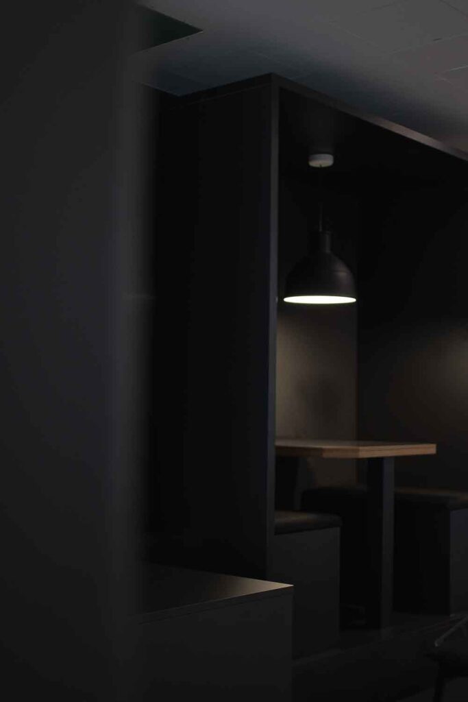 Projekt: MOIA Office – dunkel gestalteter Sitzbereich mit schwarzer Einbau-Box, Tisch und Pendelleuchte