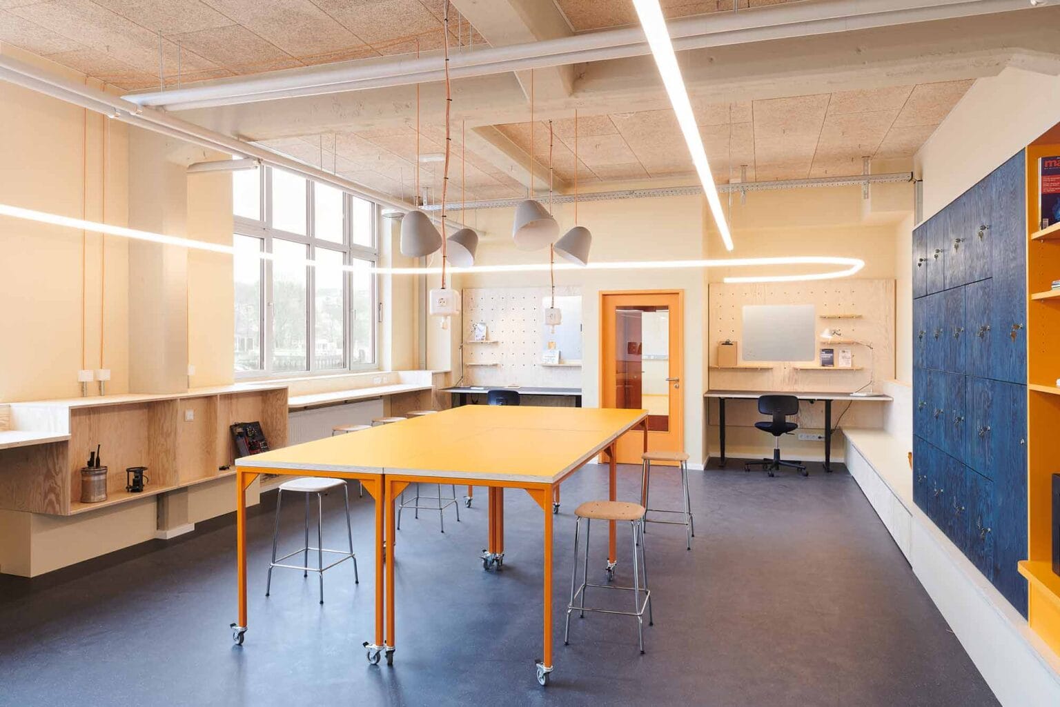 Projekt: TranMarTech SH – Werkraum mit langem Tisch, Wandregalen und blauer Schrankwand