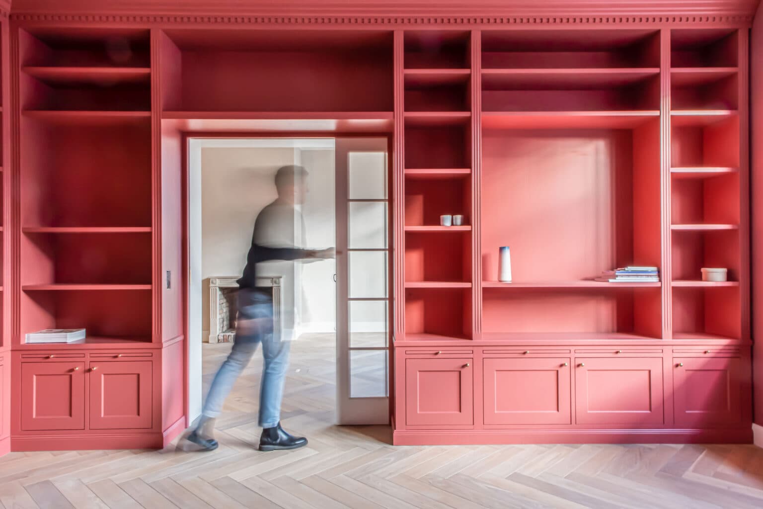 Projekt: Stadtvilla – Person geht durch den Durchgang im korallfarbenen Bibliothekenschrank