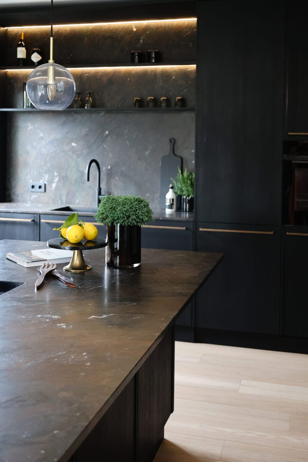 Küche: Black Kitchen – Kochinsel mit dunkler Steinplatte und beleuchtetem Wandregal