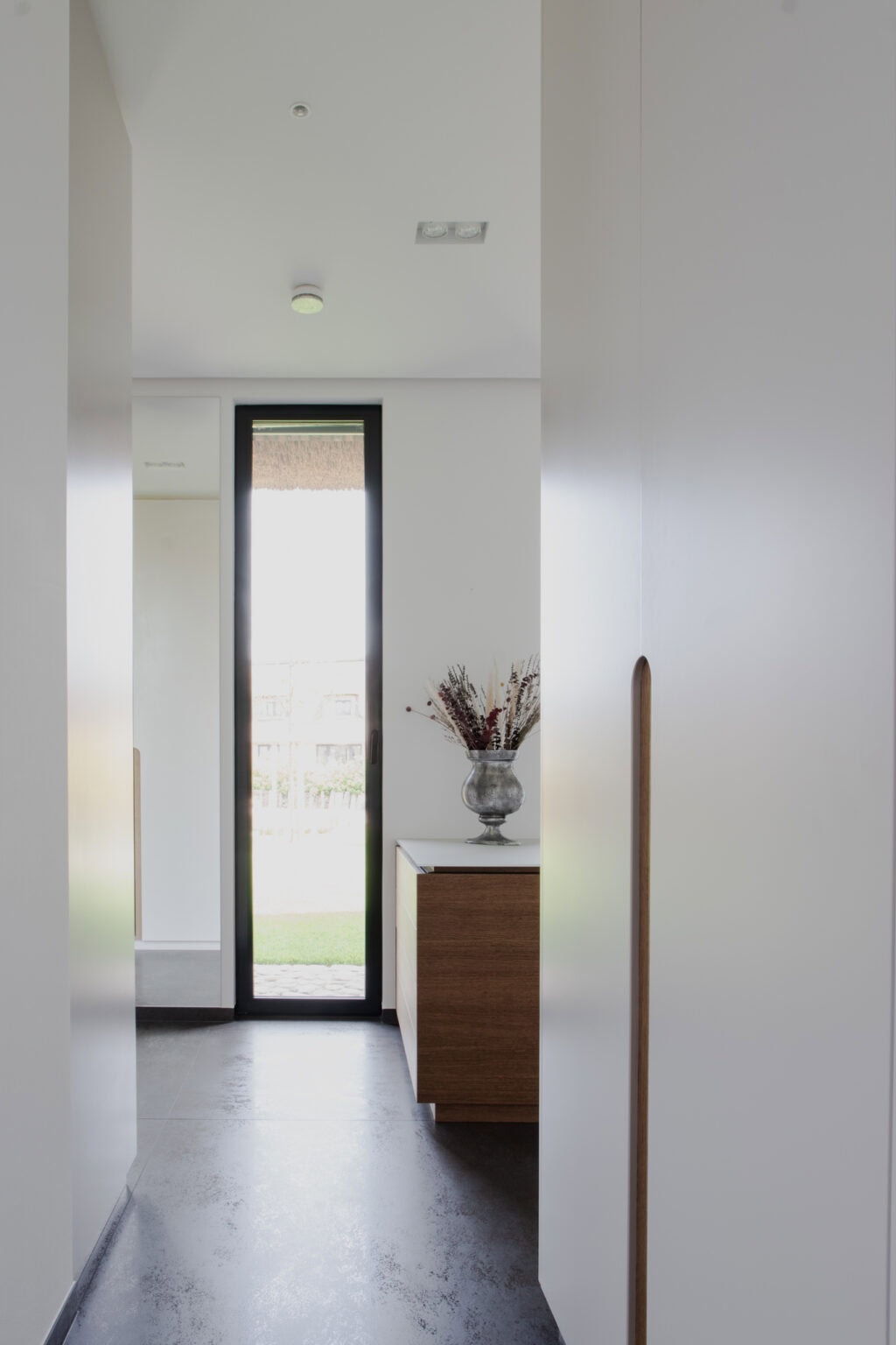 Elegantes Ankleidezimmer – Blick an grifflosen Schränken vorbei zum Fenster mit Kommode