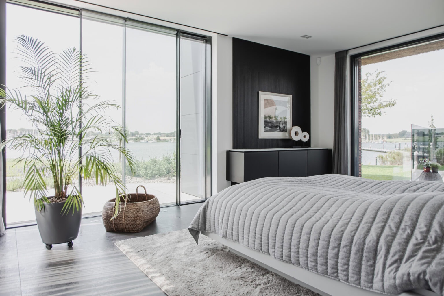 Projekt: Exklusives Wohnen an der Schlei – Schlafzimmer mit Bett und dunklem Sideboard am Fenster