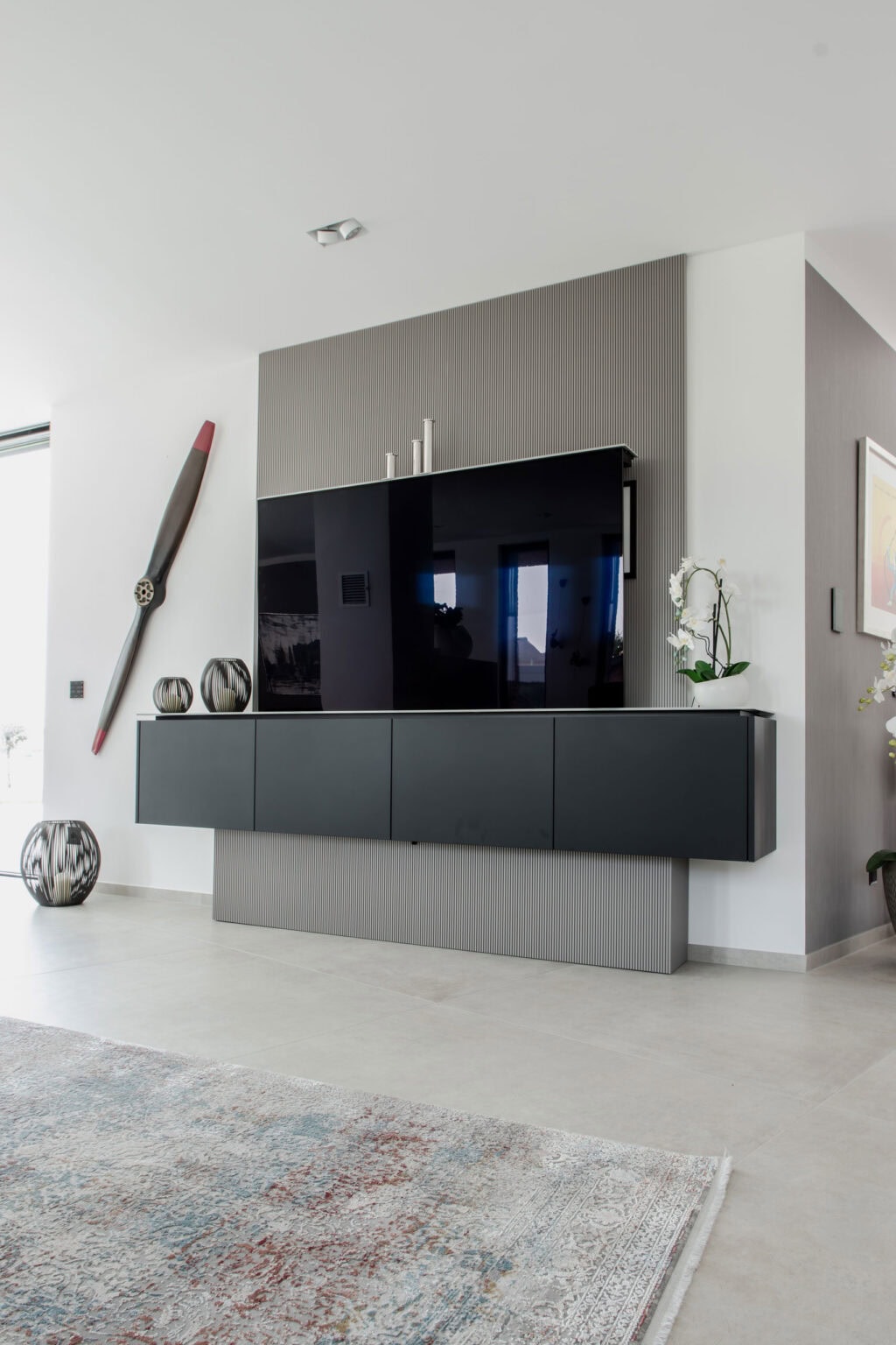 Projekt: Exklusives Wohnen an der Schlei – dunkles Lowboard mit Fernseher vor grauer Wandscheibe