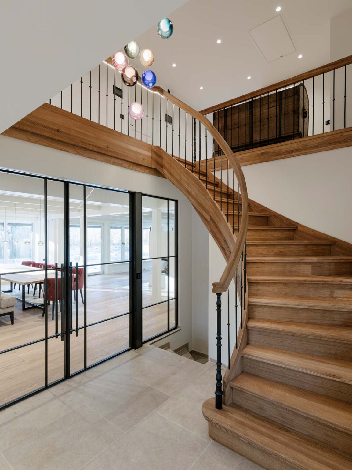 Projekt: Modernes Landhaus – geschwungene Holztreppe neben schwarzer Glaswand