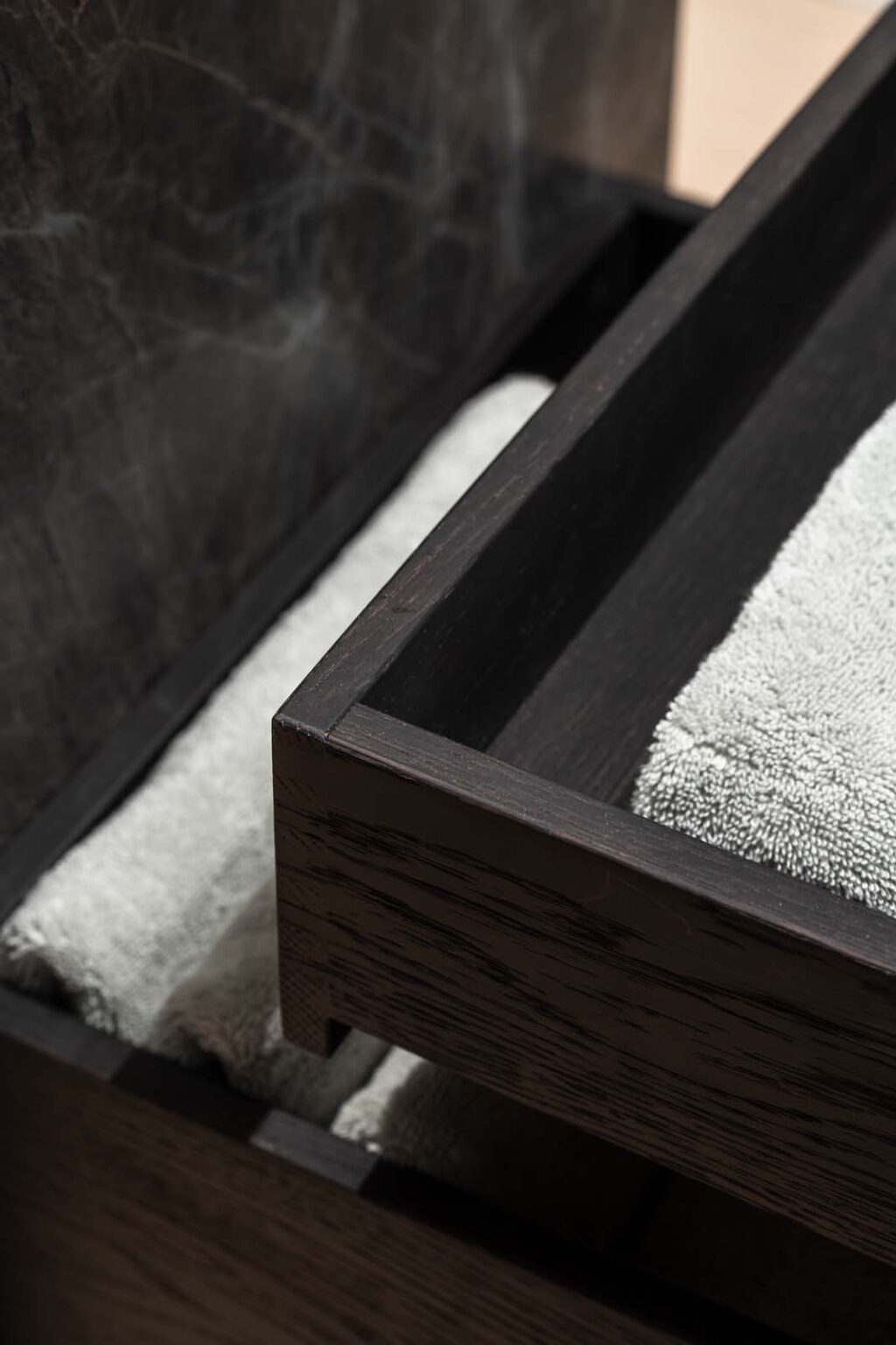 Crafted in Stone Gästebad – Detail: Handtuchfach aus dunklem Holz unter dem Waschtisch