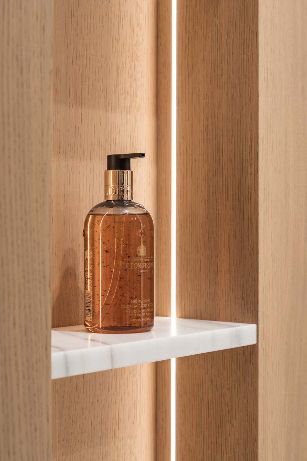 Masterbad Leise Eleganz – Detail: beleuchtete Holznische mit Seifenspender